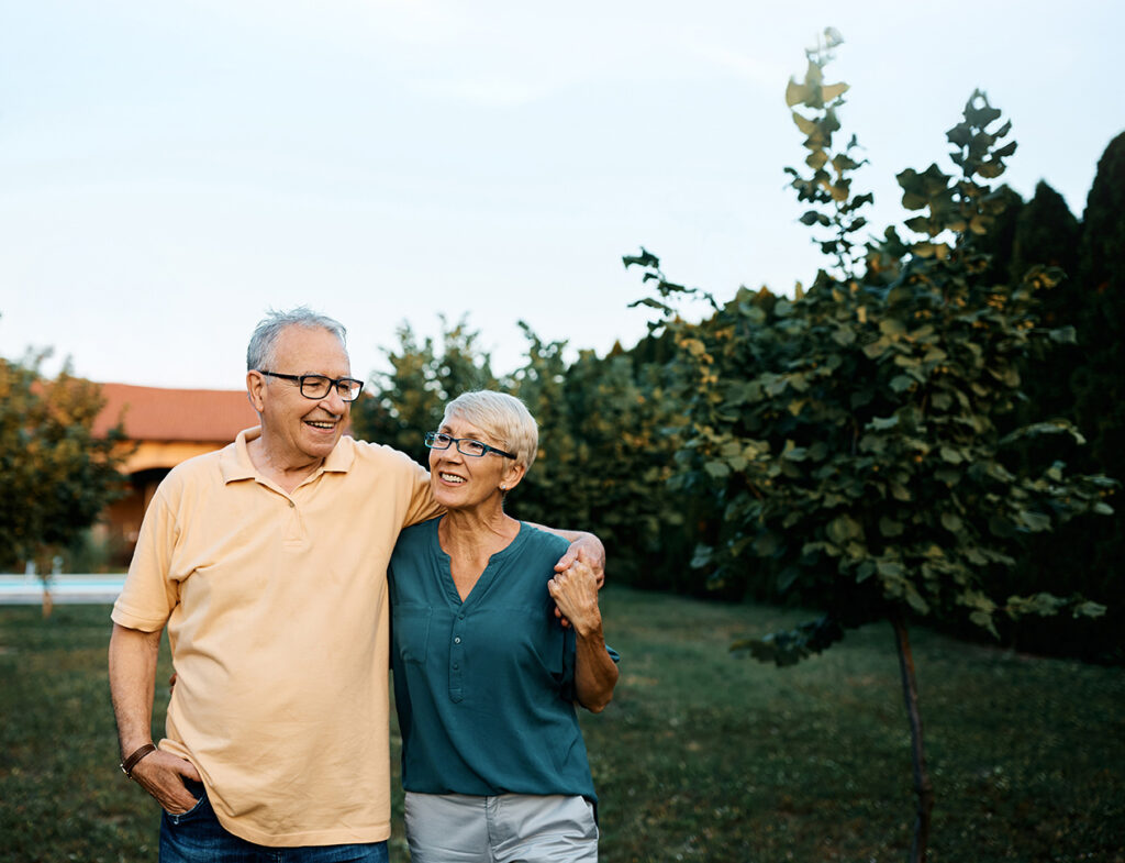 Happy senior couple enjoying while walking embraced in their backyard. Copy space.